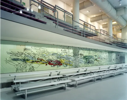 Long mural on a piece of glass behind a row of bleachers in a gym. 