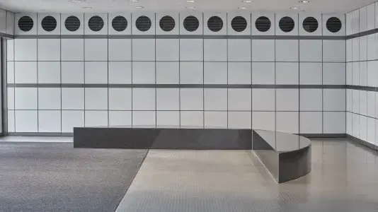 L-shaped granite bench with a black and white gridded wall in the background that has black circles lining the top row. 