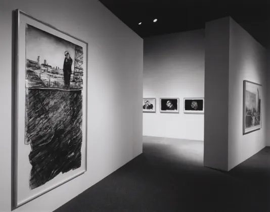 A male figure stands amidst an industrial landscape in a large, foreground drawing, 4 other drawings hang in the gallery.