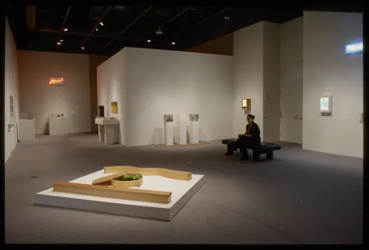 Viewer seated on a bench in a room surrounded with many objects.